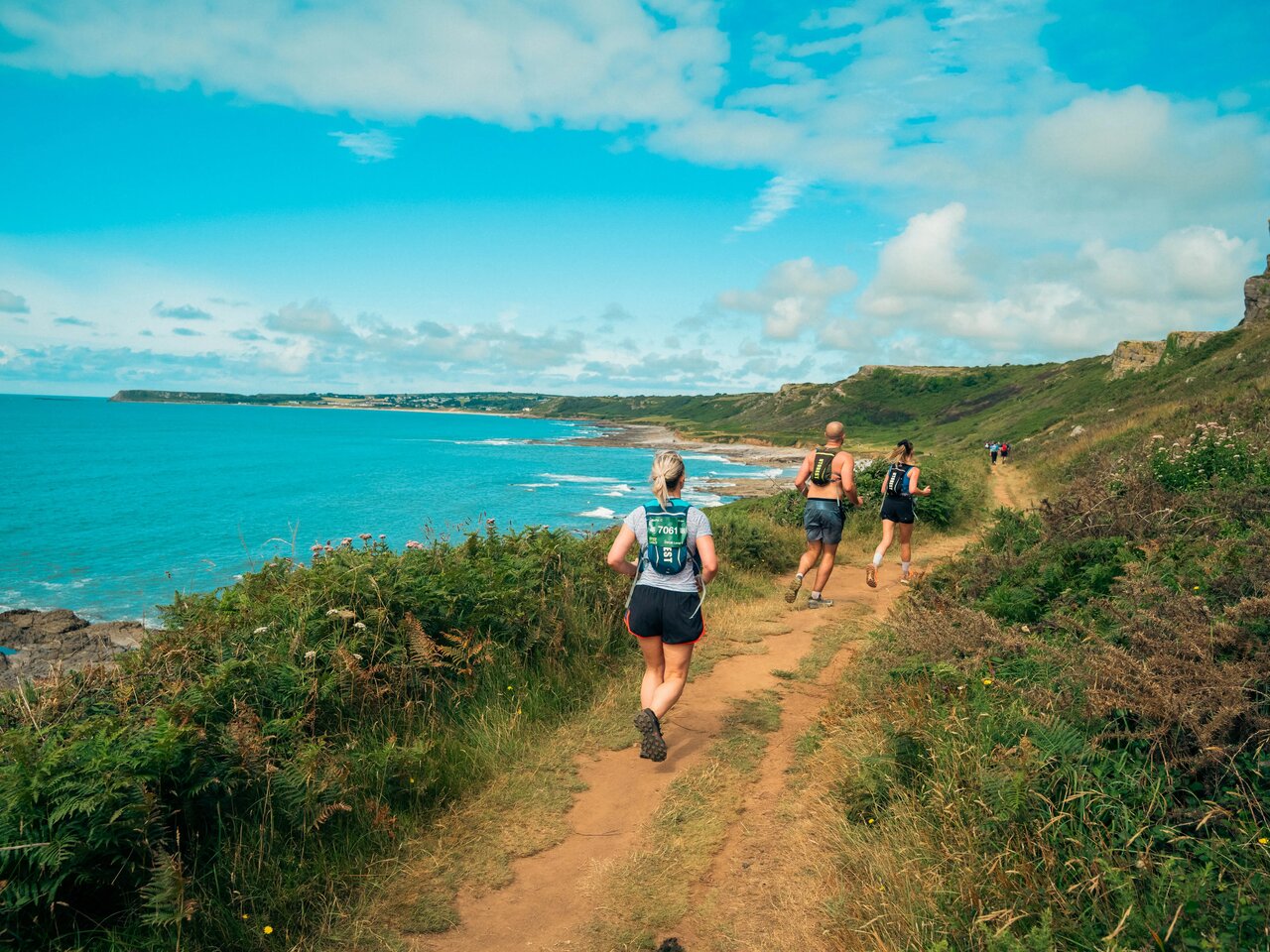 A photo of people running along a coastal path on a sunny day as part of the Gower Peninsula Ultra Challenge