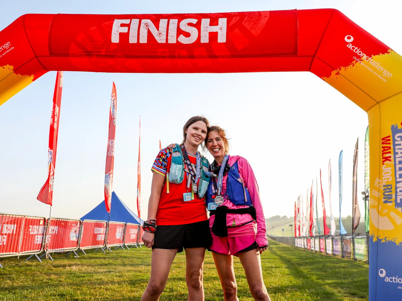 A photo of 2 women at the finish line of the North Norfolk 50 Ultra Challenge. There are both wearing medals and smiling.
